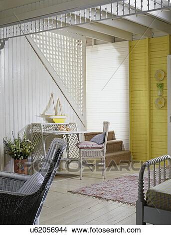 ENTRY AND HALLWAY: front hall: vacation home, painted yellow wood lath walls, white painted exposed beams, stairway with lattice, light wood floors, area rug, wicker furniture, sailboat toy cottage style, floral arrangement in painted tin bucket, wainsco View Large Photo Image Picture - ENTRY AND HALLWAY: front hall: vacation home, painted yellow wood lath walls, white painted exposed beams, stairway with lattice, light wood floors, area rug, wicker furniture, sailboat toy cottage style, floral arrangement in painted tin bucket, wainsco. Fotosearch