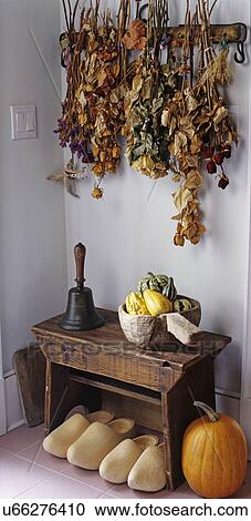 Stock Image - entry ways: area decorated with dried flowers hanging from wall, small bench with old hand bell, wooden bowl filled with gourds, Dutch shoes. Fotosearch