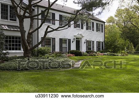 Stock Image - EXTERIOR: White brick traditional colonial home with black shutters, pediment above the door,. Fotosearch