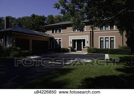 Stock Image - EXTERIORS: Brick Prairie style home, garage to left, blacktop driveway with inset pavers, planters on either side of doorway, shaded. Fotosearch