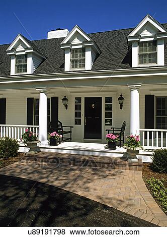 Stock Photo - EXTERIORS: Classic traditional home, white siding, black door and shutters, symmetrically placed benches and pink geraniums, brick walkway, three dormers. Fotosearch