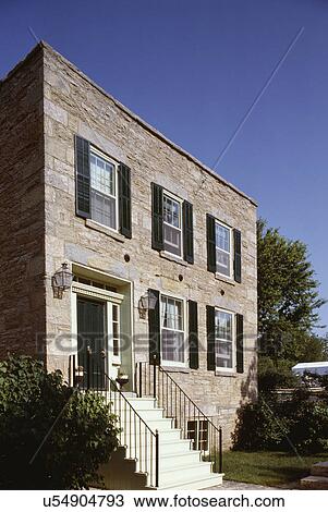 Stock Image - EXTERIORS: late Federal period stone house, dark green shutters and front door, gas look lanterns, steps to front door, English basement, flat roof. Fotosearch