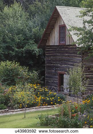 Stock Image - EXTERIORS: Log Barn near flower garden, 2-story, Scandinavian outbuilding, late summer gardens, rustic country . Fotosearch
