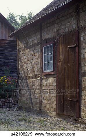 Stock Photo - EXTERIORS: Log farm buildings. Close up of shed with brick walls. Door with wide boards, Scandinavian. Fotosearch