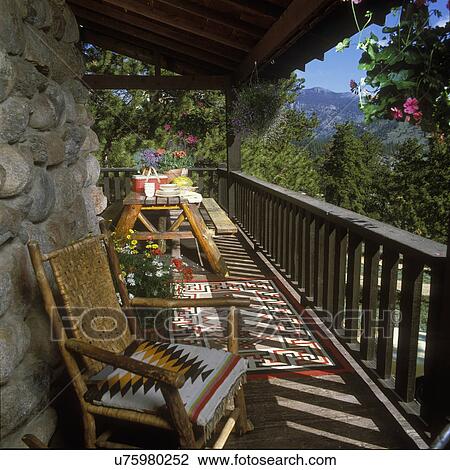EXTERIORS - Rustic Vacation home set in the Colorado Rockies, on porch overlooking the mountains, log picnic table set with lunch, foreground twig chair with woven back and rug seat, Native American rug on floor of porch, hanging flowers View Large Photo Image Stock Image - EXTERIORS - Rustic Vacation home set in the Colorado Rockies, on porch overlooking the mountains, log picnic table set with lunch, foreground twig chair with woven back and rug seat, Native American rug on floor of porch, hanging flowers. Fotosearch