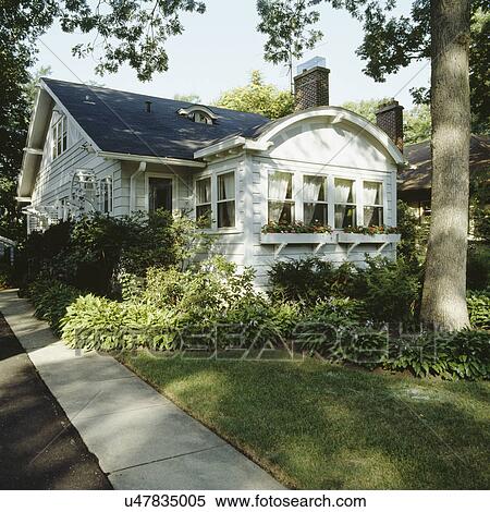 Stock Photography - EXTERIORS: single family bungalow in the city, arched sun porch area, window boxes filled with impatiens, host, concrete sidewalk to entry along side of home, angle view, narrow yard, mature trees,. Fotosearch