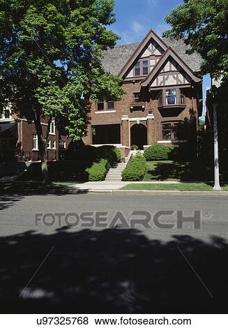 EXTERIORS: three story brick Tudor Revival home in Milwaukee Wisconsin, looking from city street to front yard with concrete steps to arched porch entry View Large Photo Image Stock Photo - EXTERIORS: three story brick Tudor Revival home in Milwaukee Wisconsin, looking from city street to front yard with concrete steps to arched porch entry. Fotosearch