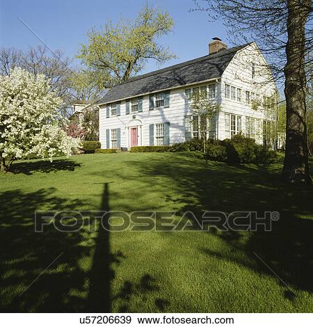 Stock Photo - EXTERIORS: two story colonial revival with turquoise shutters, large lawn, springtime flowering trees,. Fotosearch