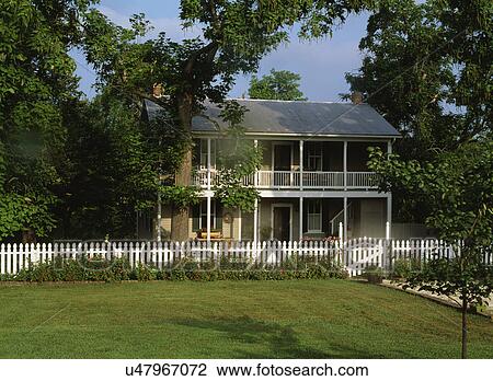 Stock Image - EXTERIORS: Two story home, white picket fence, porches on both levels run the length of the house. Fotosearch