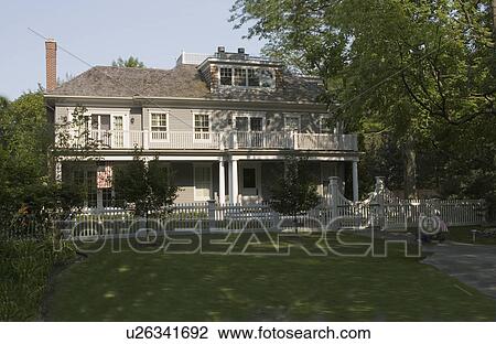 Stock Image - EXTERIORS: Two story, porch extends across the front of home, picket fence with gate, American flag hangs on the left on the lower porch. Fotosearch
