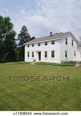 Stock Image - EXTERIORS: Two-story single family stucco Georgian Colonial farmhouse, built in 1841, restored, lawn, plain and simple, vertical version with more picket fence to right, ground cover near house. Fotosearch