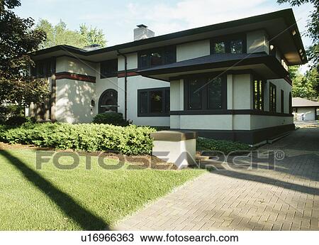 Stock Image - EXTERIORS: Two story single family home, Prairie style, remodeled stucco, brick driveway to right, angle view in shadow. Fotosearch