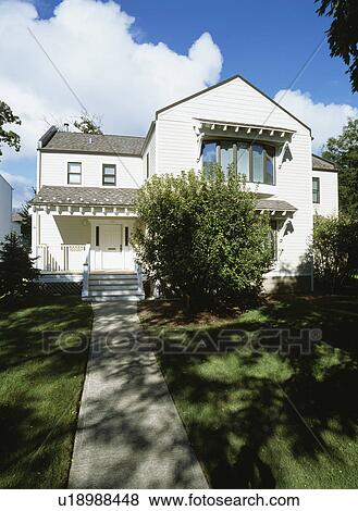 Stock Photo - EXTERIORS: Two story single family house, beige frame, wood awnings over windows, remodeled, concrete sidewalk to porch, large bush in front. Fotosearch