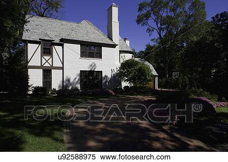 Stock Photography - EXTERIORS: White brick French Country style home, shaded yard and brick driveway. Fotosearch