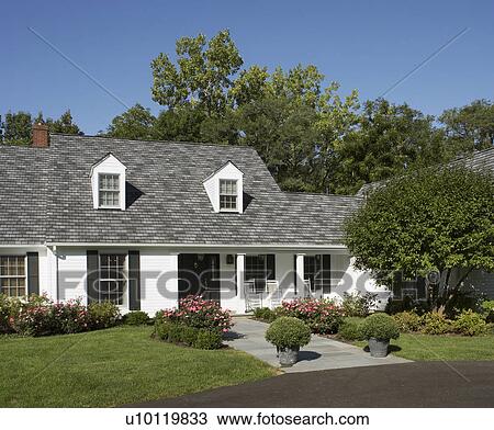 Stock Image - EXTERIORS: White traditional home with black shutters, front porch, pink rose bushes, line the slate walkway to the entrance, blacktop drive in foreground, vertical. Fotosearch