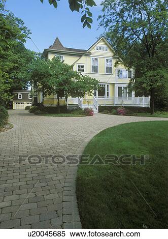 Stock Photography - EXTERIORS: Yellow clapboard Victorian with white trim, curved cobblestone driveway, three story home, detached garage, surrounded by mature trees, porch/deck in front, vertical. Fotosearch
