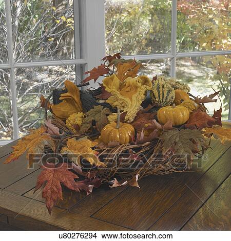 Picture - FALL SEASON: twig basket filled with gourds and pumpkins, leaves, paned windows behind, square format, more table in foreground. Fotosearch
