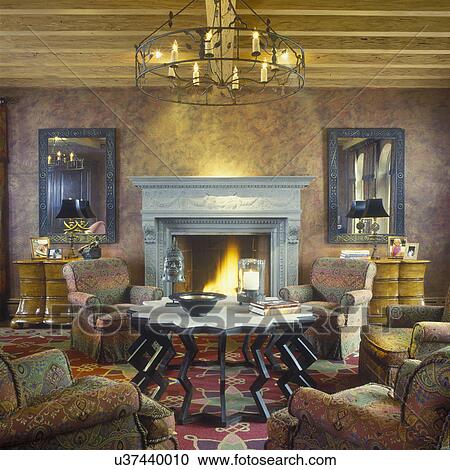 FAMILY LIVING AREA -Living Room, tall Neo-classical fireplace, symmetrically placed mirrors and Bombay style chests on either side of fireplace, large round iron chandelier, interesting shaped table, contemporary, four upholstered arm chairs, African bro View Large Photo Image Stock Image - FAMILY LIVING AREA -Living Room, tall Neo-classical fireplace, symmetrically placed mirrors and Bombay style chests on either side of fireplace, large round iron chandelier, interesting shaped table, contemporary, four upholstered arm chairs, African bro. Fotosearch