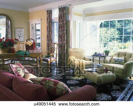FAMILY SITTING AREA - Bay window, yellow walls, white trim, black area rug, yellow upholstered armchairs and ottoman, backside of paprika sofa, large mirror to left, geraniums, ring top drapes in red, traditional, View Large Photo Image Stock Photography - FAMILY SITTING AREA - Bay window, yellow walls, white trim, black area rug, yellow upholstered armchairs and ottoman, backside of paprika sofa, large mirror to left, geraniums, ring top drapes in red, traditional,. Fotosearch