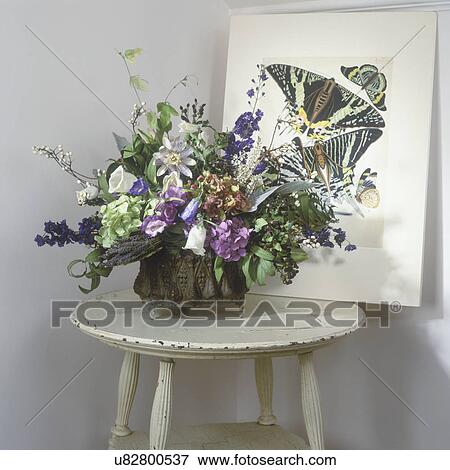 FLOWER ARRANGEMENTS: Dried flower arrangement on a white distressed table, shades of greens, whites. Hydrangeas, Bellflowers, lavender, delphinium, tallow berry, clematis, butterfly print behind View Large Photo Image Stock Photo - FLOWER ARRANGEMENTS: Dried flower arrangement on a white distressed table, shades of greens, whites. Hydrangeas, Bellflowers, lavender, delphinium, tallow berry, clematis, butterfly print behind. Fotosearch