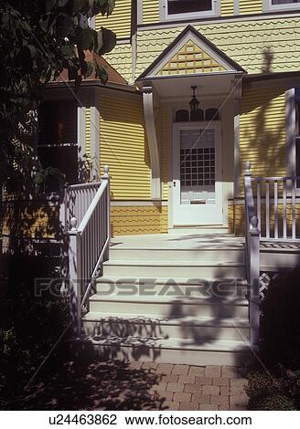 Stock Image - FRONT DOORS: Exterior of front entrance, white trim and wooden steps to deck, architectural details and various trim work, remodeled Victorian, 2 shades of yellow,. Fotosearch