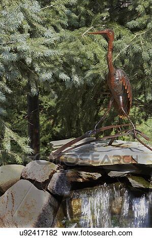 Stock Image - GARDEN: DETAIL, top of waterfall, rusty blue heron sculpture. Fotosearch