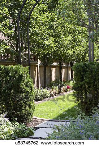 Stock Image - GARDEN: Looking through arbor to wood privacy fence with tree line, flower border. Fotosearch