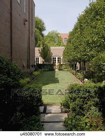 Stock Image - GARDEN: Narrow city yard, trees line one side, brick home to right, and brick garage to back of lot. Fotosearch