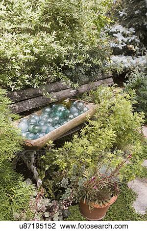 GARDEN: Park bench almost covered by shrubs, wooden bowl filled with blue glass balls, terra cotta pot View Large Photo Image Stock Image - GARDEN: Park bench almost covered by shrubs, wooden bowl filled with blue glass balls, terra cotta pot. Fotosearch