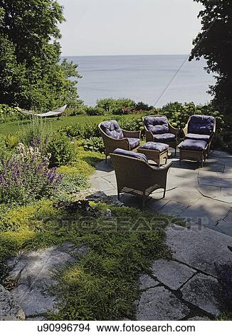 Picture - GARDEN/ PATIO: Terraced stone patio and walkway overlooking water views and garden, wicker patio furniture, hammock. Fotosearch