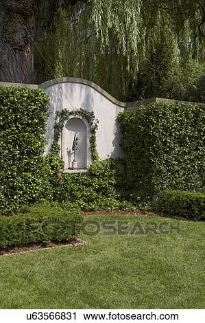 Stock Image - GARDENS: garden wall, niche with statue, shaped hedges surround, lawn to foreground, large willow tree to back. Fotosearch