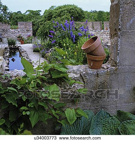 Gardens: Looking into free-flowing flower garden created inside stone foundation of demolished barn, small reflecting pool, tall purple flowers, clay pots. View Large Photo Image Stock Image - Gardens: Looking into free-flowing flower garden created inside stone foundation of demolished barn, small reflecting pool, tall purple flowers, clay pots.. Fotosearch