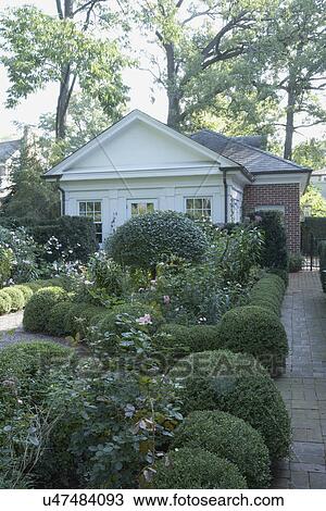 Stock Image - GARDENS: Shaped boxwood hedges and rose gardens lead to a classical styled potting shed attached to a brick garage. Fotosearch