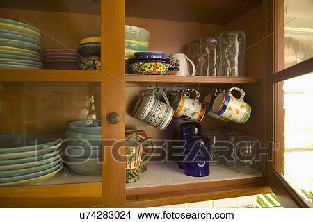 Glass Front Cabinet With Stacks Of Dishware And Hanging Coffee