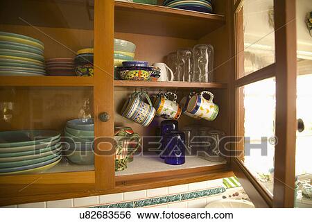 Glass front cabinet with stacks of dishware and hanging coffee mugs; Carpinteria; California; USA View Large Photo Image Stock Photograph - Glass front cabinet with stacks of dishware and hanging coffee mugs; Carpinteria; California; USA. Fotosearch