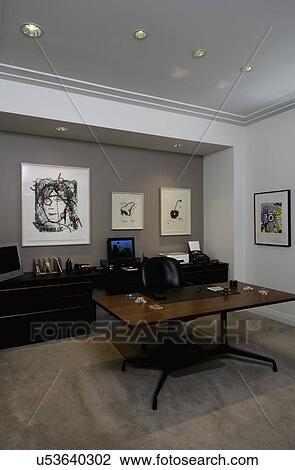 Stock Image - HOME OFFICE: contemporary home office, clean lined desk and back work area with computer, 20thc art prints crown molding of plaster. Fotosearch