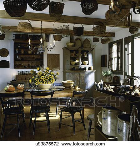 Stock Image - KITCHEN Country. Antique table baskets, shelves, dining area with dining table and chairs, candle chandelier. Fotosearch