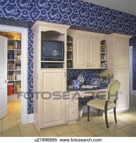 KITCHEN DESK AREA: Built-in desk area, with cabinets, shelving, and TV. Tan ceramic tile floor. Dark blue and white botanical patterned wall paper. Door on left leads to pantry. View Large Photo Image Stock Photography - KITCHEN DESK AREA: Built-in desk area, with cabinets, shelving, and TV. Tan ceramic tile floor. Dark blue and white botanical patterned wall paper. Door on left leads to pantry. . Fotosearch