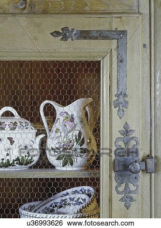 KITCHEN DETAIL: Antique cupboard, scoll metal hinge and latch, wire mesh door front, square nail construction, Portmeirion Welsh Pottery View Large Photo Image Stock Photograph - KITCHEN DETAIL: Antique cupboard, scoll metal hinge and latch, wire mesh door front, square nail construction, Portmeirion Welsh Pottery. Fotosearch