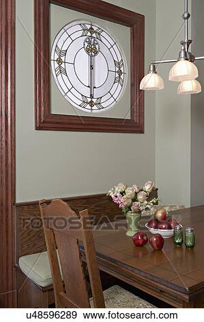 Stock Photo - KITCHEN EATING AREA: built in breakfast nook with square stained glass window, chandelier, bowl of apples, floral arrangement, salt and pepper shakers, more chandelier and chair showing. Fotosearch