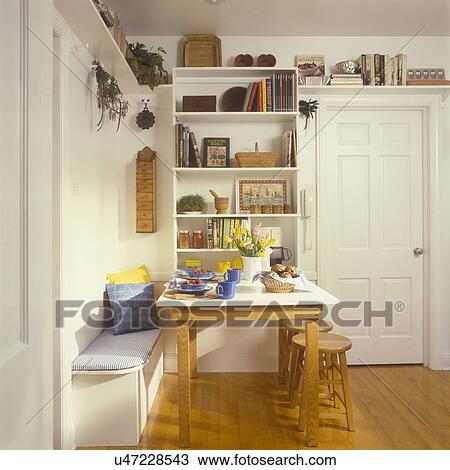 KITCHEN - eating area has shelf unit attached to wall with gallery shelf above it and over door. Oak table pulls out lid lifts on banquette below for storage, stools, built in seat, storage in small spaces View Large Photo Image Stock Image - KITCHEN - eating area has shelf unit attached to wall with gallery shelf above it and over door. Oak table pulls out lid lifts on banquette below for storage, stools, built in seat, storage in small spaces. Fotosearch