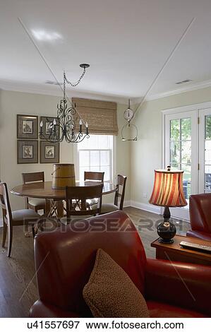 KITCHEN EATING AREA: View toward eating area in great room layout, traditional, round table and chairs, iron chandelier, framed photos on wall, striped shade on table lamp, wood floor, red leather club chair in foreground, antique scale hangs in corner, View Large Photo Image Stock Photo - KITCHEN EATING AREA: View toward eating area in great room layout, traditional, round table and chairs, iron chandelier, framed photos on wall, striped shade on table lamp, wood floor, red leather club chair in foreground, antique scale hangs in corner, . Fotosearch
