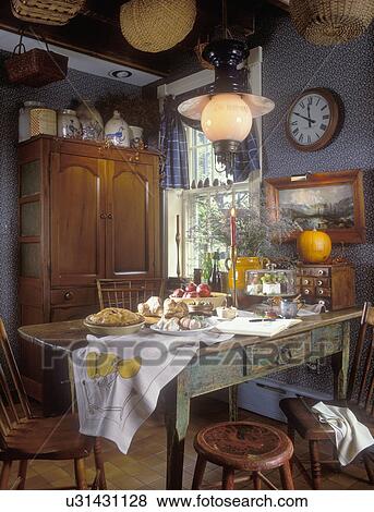 Stock Photo - KITCHEN EATING AREAS - 19th century antiques and collections. Traditional American. Original paint on 1800's dining table, fall meal preparations, pie, pomegranates, pumpkin, blue wallpaper, blue and white checkered valance, maple cupboard, antique stonew. Fotosearch