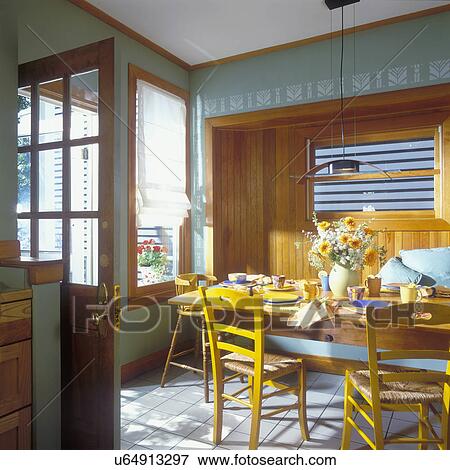 Stock Photo - KITCHEN EATING AREAS: Contemporary look, a recessed bead-board bench seat under frosted glass window, long plank table with chairs, sage green walls, white stenciling.. Fotosearch
