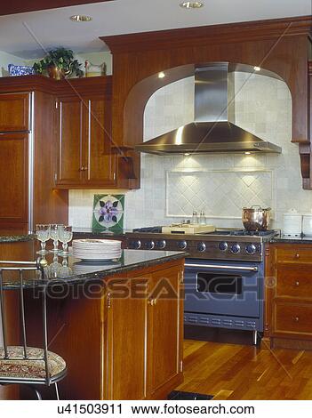 KITCHEN - Partial view of island and stove area with exhaust hood, commercial stainless steel, cherry wood cabinetry, granite tops. View Large Photo Image Stock Image - KITCHEN - Partial view of island and stove area with exhaust hood, commercial stainless steel, cherry wood cabinetry, granite tops.. Fotosearch