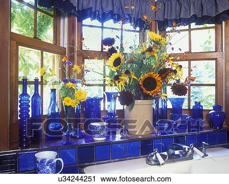 Stock Image - KITCHEN SINK AREA DETAILS: Log House Detail, sink, cobalt blue glassware, in window well of bay window, crock filled with sunflowers . Fotosearch
