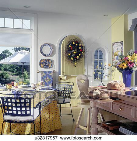 Stock Photo - KITCHENS: Breakfast area, yellow Dutch door to patio, Country French pattern tablecloth, metal chairs, sliced bread on center island, vase of flowers, wreath on door. Fotosearch