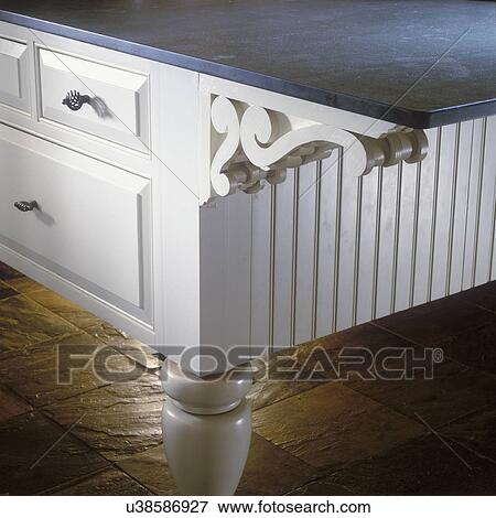 Stock Photo - KITCHENS - Detail shot of kitchen island with krikstone top, wooden base, a carved scroll corbel supports countertop, slate flooring.. Fotosearch