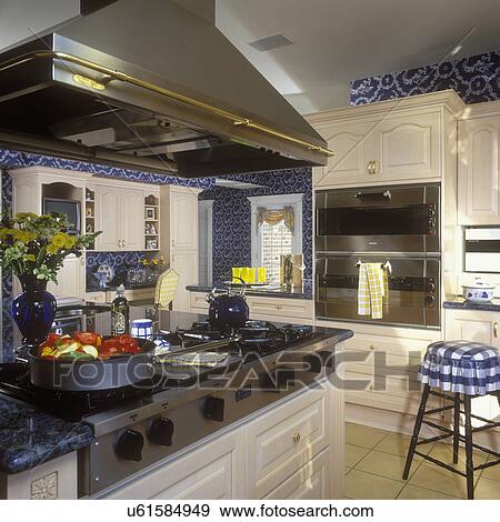 KITCHENS: Gas stove top area with stainless steel hood, in stainless steel ovens on right. Pickled white cabinets. Far wall has dark blue pattern wall paper. Kitchen desk area. View Large Photo Image Stock Photo - KITCHENS: Gas stove top area with stainless steel hood, in stainless steel ovens on right. Pickled white cabinets. Far wall has dark blue pattern wall paper. Kitchen desk area. . Fotosearch