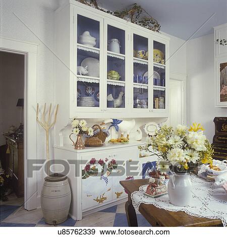 KITCHENS - Painted cabinet in country kitchen, lace tablecloth, faux painted geese, old wooden pitchfork, painted blue interior of cabinets, stoneware water container, gerbera floral arrangements, blue and white painted checked floors View Large Photo Image Stock Photo - KITCHENS - Painted cabinet in country kitchen, lace tablecloth, faux painted geese, old wooden pitchfork, painted blue interior of cabinets, stoneware water container, gerbera floral arrangements, blue and white painted checked floors. Fotosearch